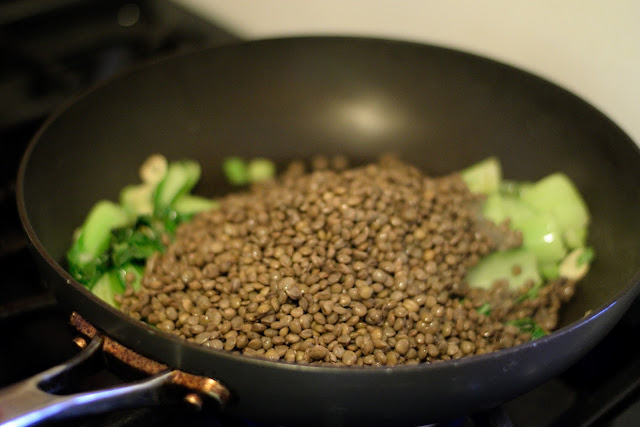 The lentils being added to the frying pan with the bok choy, green onions, and garlic. 