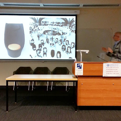 Geoff Isaac giving a talk in front of a slide of a Talking Chair by Grant Featherston and one of them in use at the 1967 World Expo.