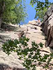 I am on a rope nearing the top of a rocky bluff. There are a few trees along the edges.