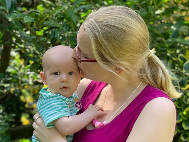 A mum holding Baby boy and wearing a Mollie & Me necklace