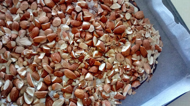 a close up of chopped toasted almonds covering the meted chocolate in a parchment lined sheet pan