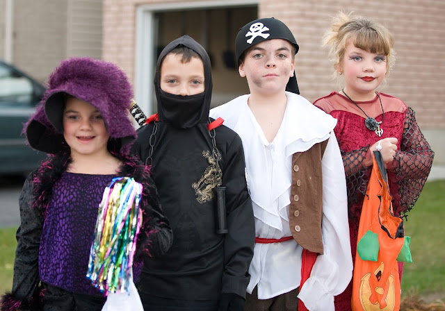 Four kids dressed up and ready for trick or treating on Halloween.