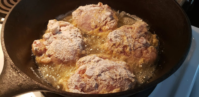 Black cast iron skillet with four pieces of chicken cooking