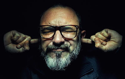 Middle-aged man with glasses, eyes shut and fingers in ears