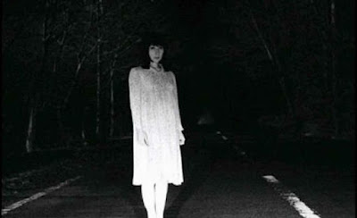 Imagem: google imagens. #PraCegoVer: mulher de branco com aspecto fantasmagórico no meio de avenida escura, durante a noite.