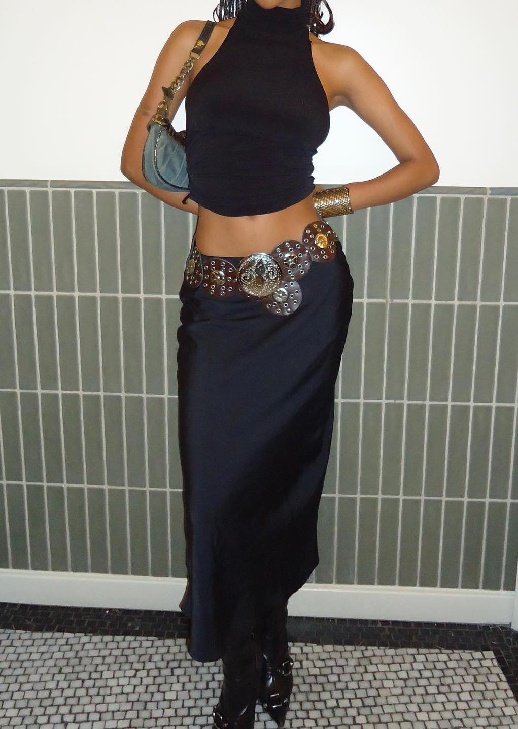 Woman with braids wearing black satin maxi skirt and a brown leather Concho disc belt and carrying a small 90s denim baguette bag