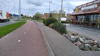 A two way cycle track and footway to the right crossing a right turn for traffic coming from the left which is controlled by traffic signals.