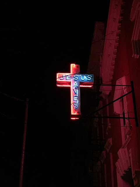 a lighted cross with the words "Jesus Saves" on it that is a sign possibly attached to a building.