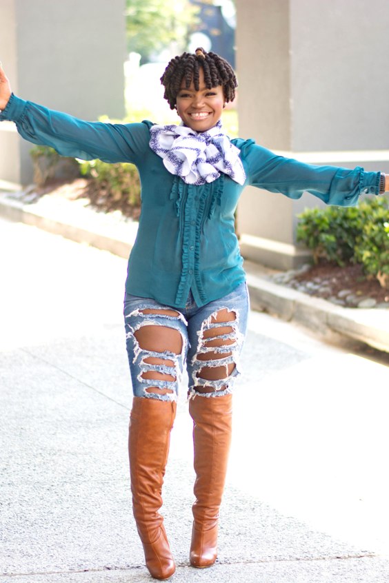 Woman wearing a green top, ripped jeans and brown over the knee boots