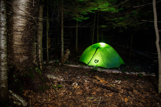 The NEMO Dragonfly 2P tent glowing green with light in a dark forest at night.