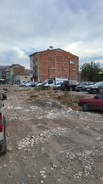 Damaged building with cracked walls and debris-filled vacant lot used as parking area in post-earthquake Malatya