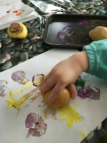 toddlers hand holding potato pressing onto a sheet of paper with potato printing on it