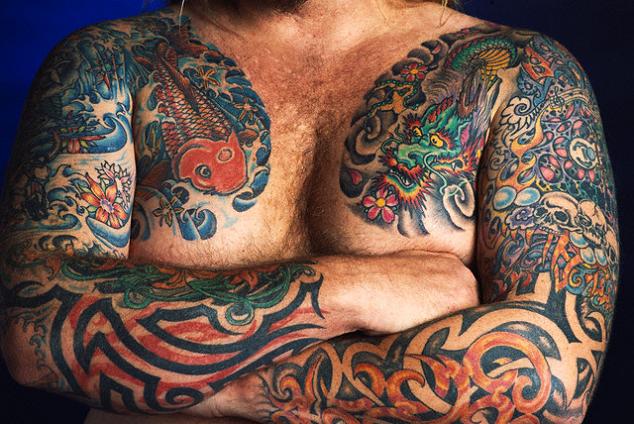 A man body tattooed with koi, flowers, skulls, tribal, and dragon tattoo.