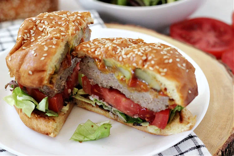 Juicy Grilled Ground Pork Burger topped with all the fixings cut in half on a white plate