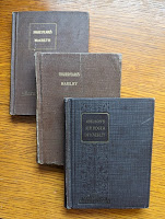 Three old school books layered on top of each other. The covers are all brownish fabric. The two underneath have gold titles of Shakespeare's MacBeth and Shakespeare's Hamlet. The top book is Addison's Sir Roger De Coverley
