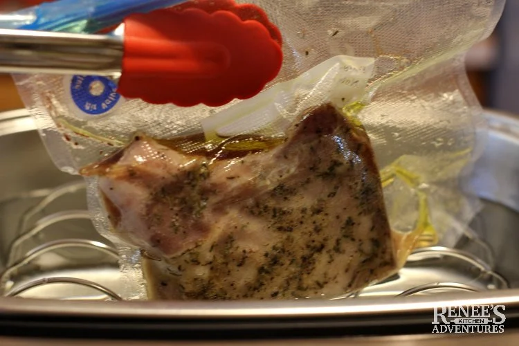 removing cooked pork chop from sous vide machine with red thongs.