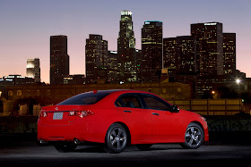 Rear three-quarters view of red 2012 Acura TSX on rooftop garage at dusk with downtown Los Angeles skyline