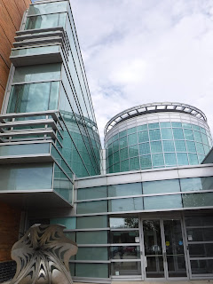 front entrance of the Sioux City Art Center, showing many rectangular glass panels set in stainless steel, with the round glass and steel atrium visible.