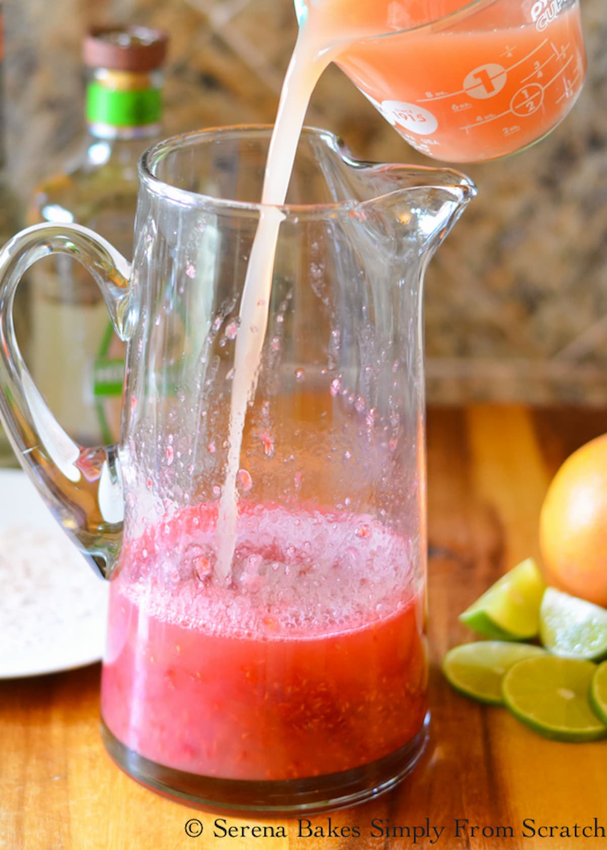 Pink Grapefruit Juice being poured into Raspberry Margarita mixture in a glass pitcher.