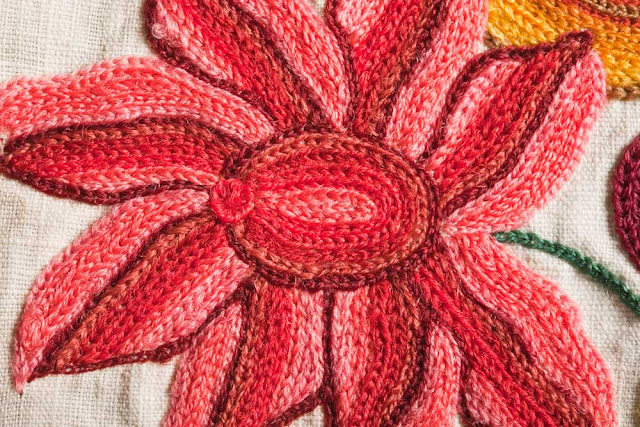 A detail of the chain stitching on a red flower, showing the neatly contoured lines of stitching in each petal and the careful shading done with thread color changes.