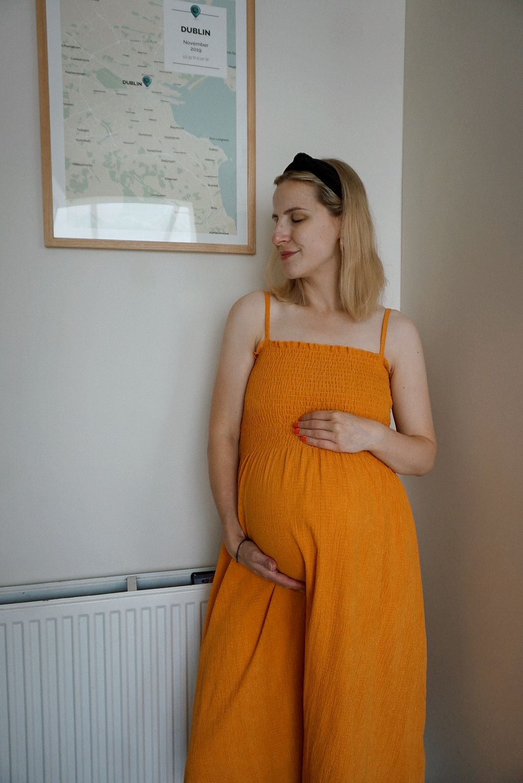 Outfit photo: Amy is wearing a bright yellow/orange sleeveless floaty dress and holding her bump