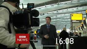Gardner stand using a zimmer in what looks like an airport screengrabed from the countdown to the hour on the BBC News channel