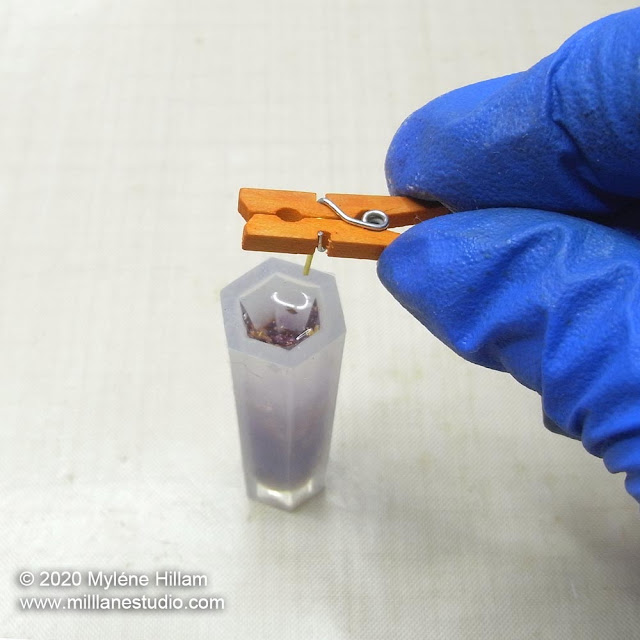 Miniature orange peg holding a gold eye pin, being inserted into a column mould filled with resin