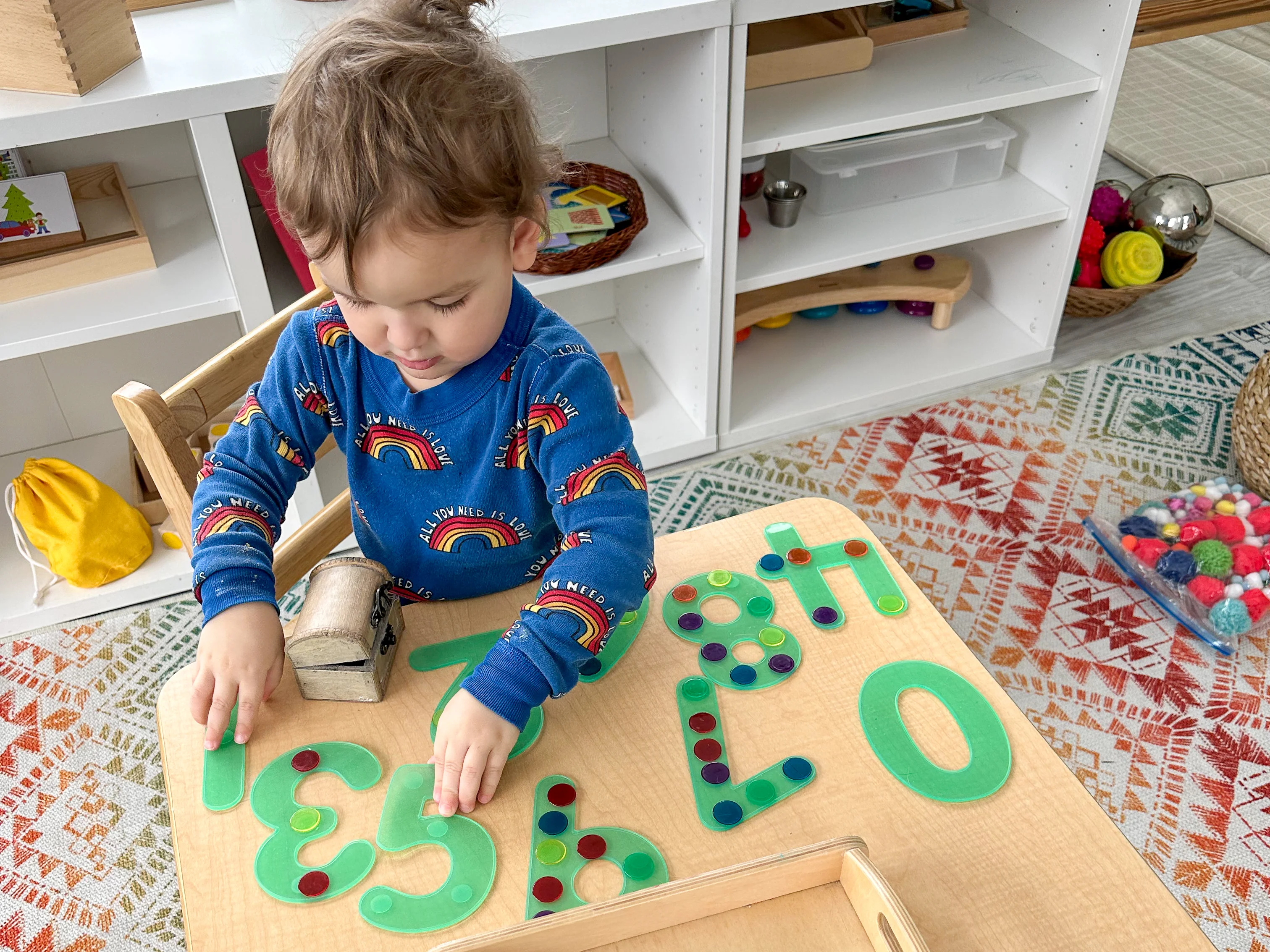 Montessori preschooler sits at home and places colorful chip counters on top of silicone number symbols as he learns to count.