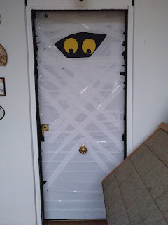 Puerta principal vestida de Momia, con dos ojos amarillos sobresaliendo entre papel higiénico.