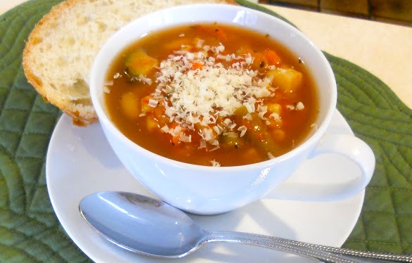 A cup of minestrone soup topped with Parmesan cheese.
