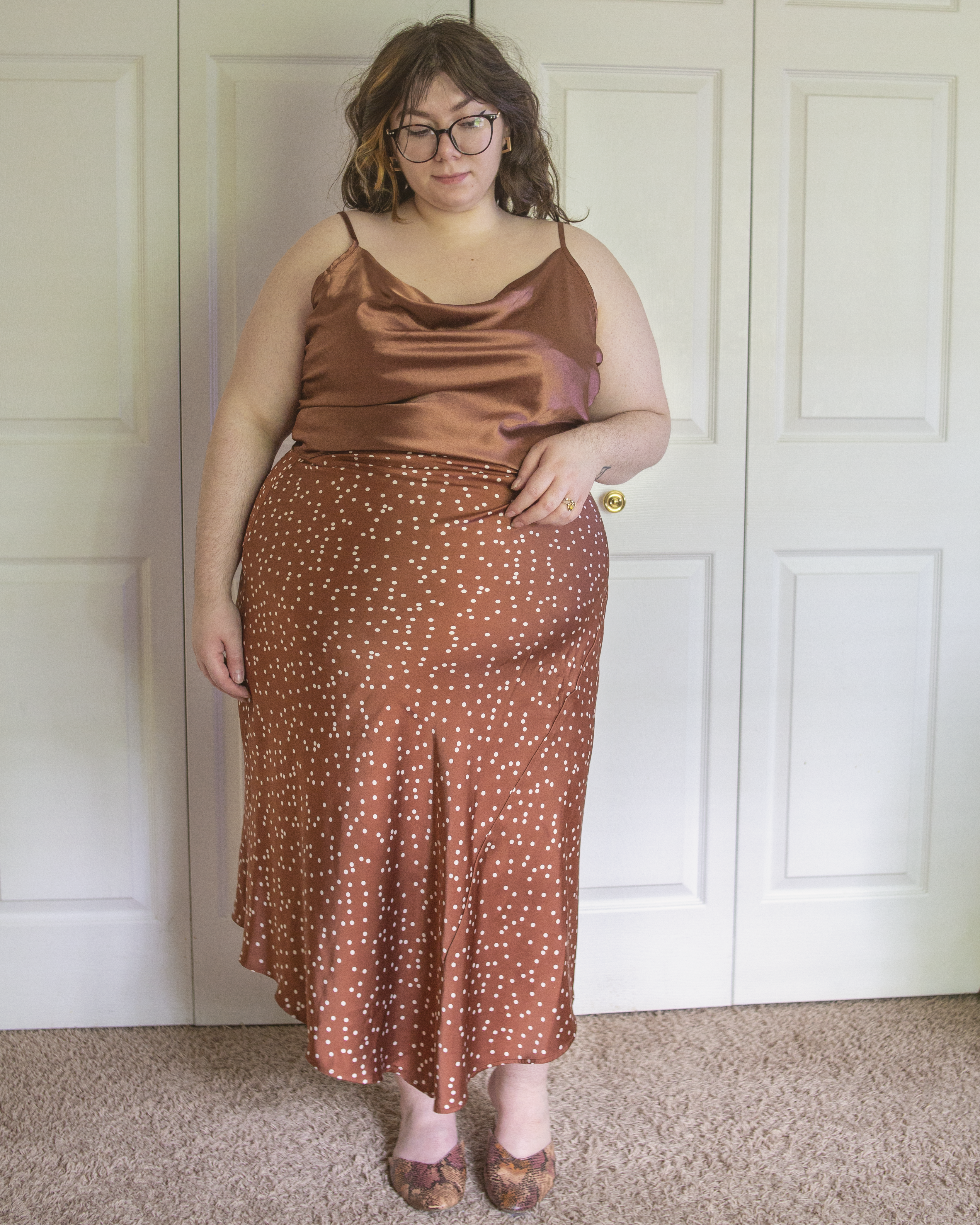 An outfit consisting of a deep dusty rose cropped satin camisole and a deep dusty rose satin slip skirt with white polka dots and assymetrical hem and dusty rose, orange and grey faux snake print mules.