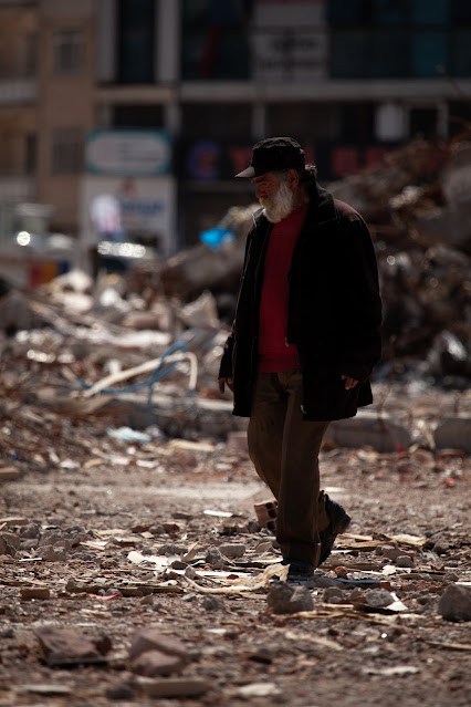 An elderly man walking upon rubble in a city