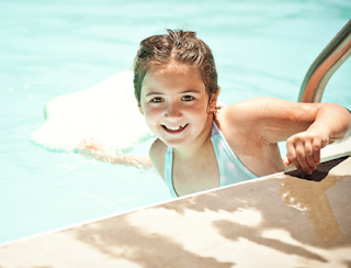 Image of happy girl with a kick board in the pool ready to swim for her children swimming lessons