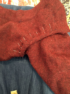 A close-up of the instep seam, rolled over and pinned wtih the points of the pins fanning out toward the ankle and leg of the hose. The fabric looks brick red against the photographer's denim skirt.