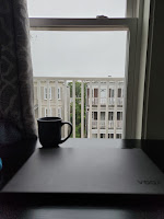 Cup of coffee and a closed laptop on a table looking out a window. It's a gray day and everything is gray and black.
