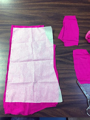 A tracing paper shirt pattern laid out on screaming magenta fabric, which sticks out at top and bottom, but the tracing paper extends past the fabric at two corners.