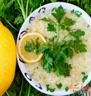 This image shows a bowl of the finished Greek Lemon Rice Soup, with a slice of lemon and a sprig of parsley as garnish. The soup is creamy and rich, with small bits of rice visible throughout. The yellow color of the soup and the vibrant green of the parsley create a visually appealing and appetizing presentation.