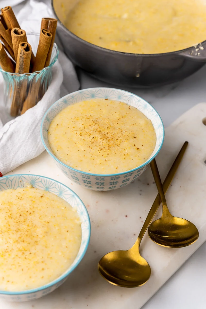 Two bowls of cornmeal porridge with spoons and cinnamon sticks.