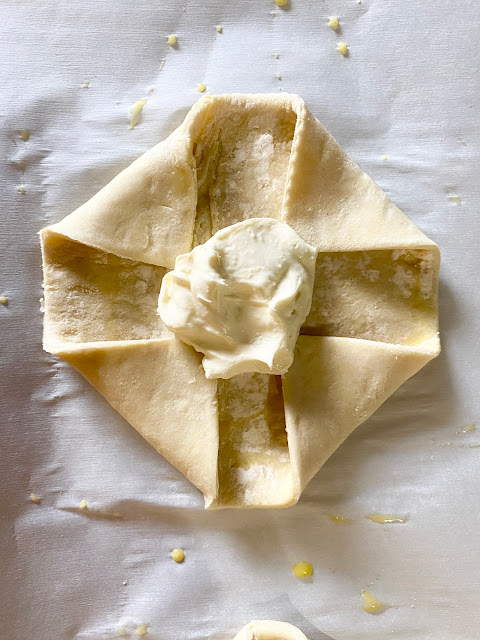 Folded puff pastry with cream cheese on parchment paper.