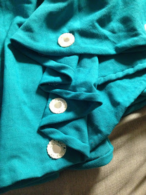 Three small round mirrors attached to the hem of a turquoise skirt with loose white shisha embroidery.