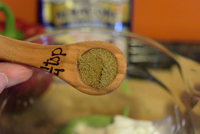 A measuring spoon over a bowl with cumin in it. 