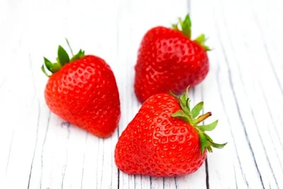 3 fresh strawberries on a whitewashed board