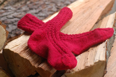 Red wool socks in Broad Spiral Rib, displayed on the woodpile