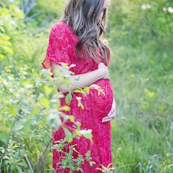 Diet for pregnant women . Standing in a green grassy field is a pregnant woman wearing a long dress.