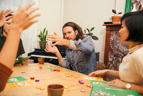 A group of people at a table with cards and tokens, all playing animatedly.