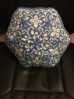 A hexagonal pillow with a floral pattern in white on a blue background. It has a blue rounded edging.