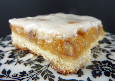 Bar cookie filled with crushed pineapple and pecans, topped with a lemon juice/powdered sugar glaze. Photographed on a white and black plate.