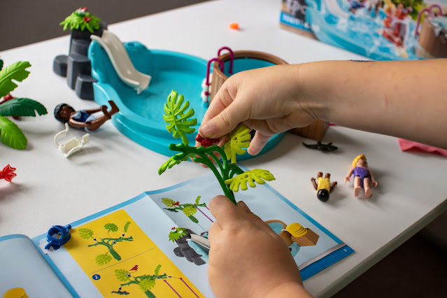 A close up of a child's hands putting leaves on a tree in front of the instructions for the Playmobil children's pool