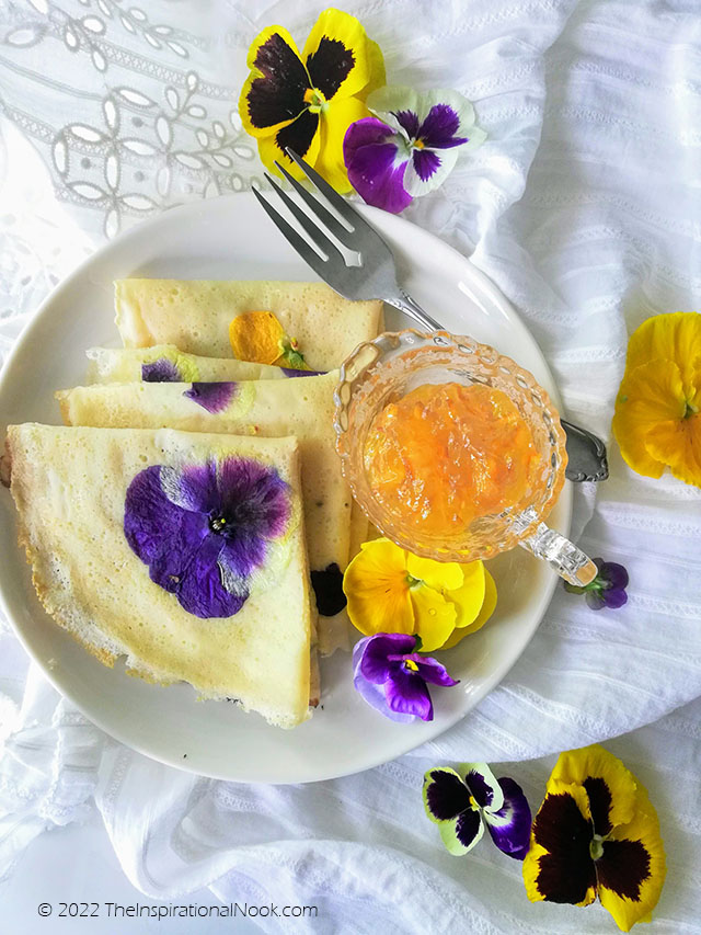 Pancakes with purple and yellow pansies and violas, flower crepes on a white plate and lace cloth