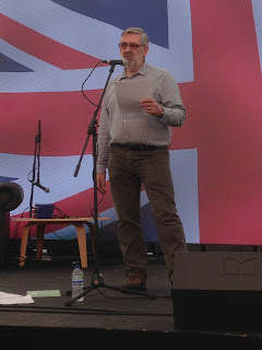 Photo of Seamus reading in front of very large Union Jack projected on screen